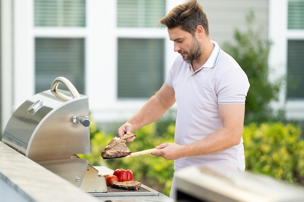 Uomo che cucina carne sul barbecue nel cortile della casa bell'uomo che prepara il barbecue barbecue c