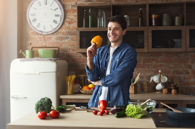 Uomo che cucina cibo delizioso e sano nella cucina soppalcata a casa in una giornata di sole. Preparazione dell'insalata di verdure.