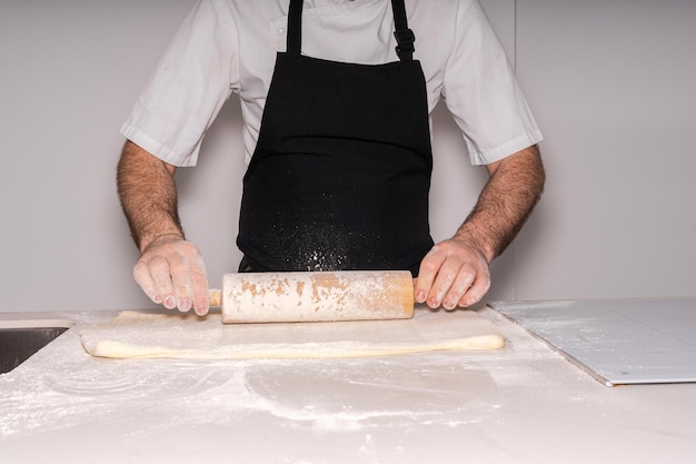 Uomo che cucina croissant fatti in casa preparando la pasta sfoglia e aggiungendo farina e appiattendola