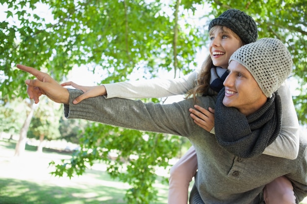 Uomo che dà la sua bella ragazza un piggy back e indicando nel parco