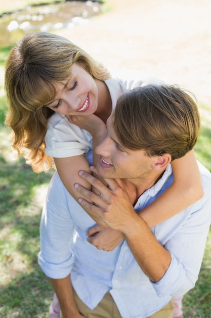 Uomo che dà la sua bella ragazza un piggy back nel parco sorridendo a vicenda