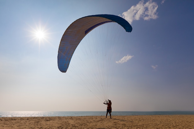 Uomo che decolla con il paracadute ascensionale sulla spiaggia soleggiata