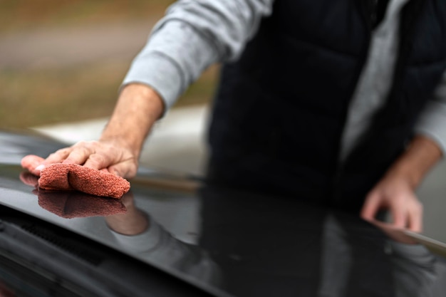 Uomo che dettaglia l'auto tenendo in mano il panno in microfibra e lucidando l'auto Messa a fuoco selettiva