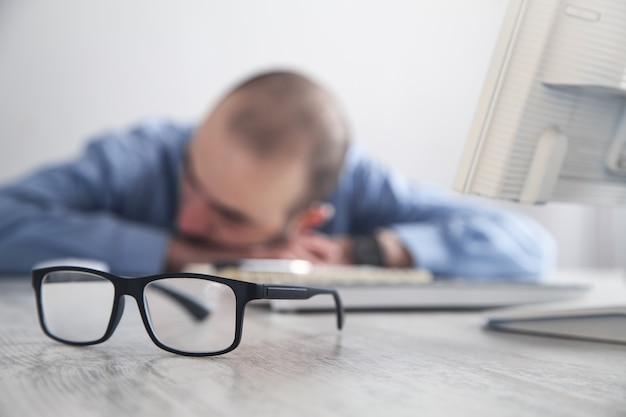 Uomo che dorme sul posto di lavoro in ufficio.