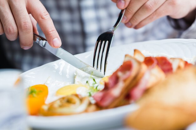 Uomo che fa colazione con forchetta e coltello, primo piano