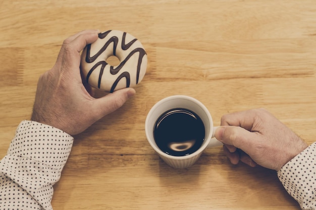 Uomo che fa colazione con una tazza di caffè e una ciambella su un tavolo di legno