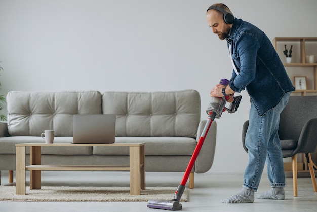 Uomo che fa i lavori domestici con l'aspirapolvere ad accumulatore e ascolta la musica in cuffia