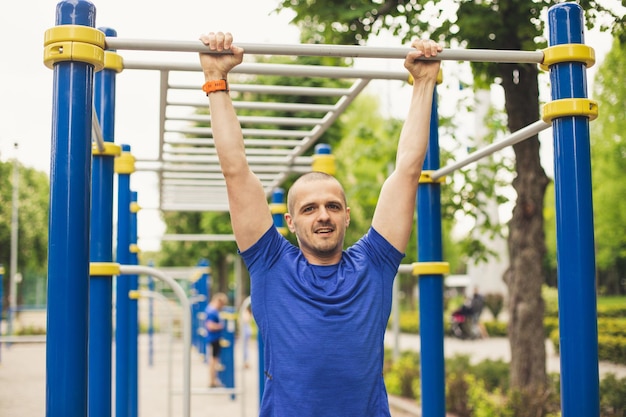 Uomo che fa pull up allenamento nel parco. Vestito con una maglietta blu e guardando a porte chiuse