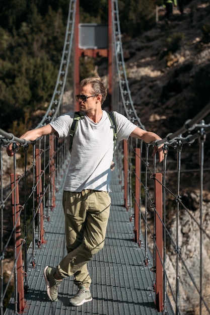 Uomo che fa un'escursione in montagna con lo zaino in piedi sul ponte in una giornata di sole