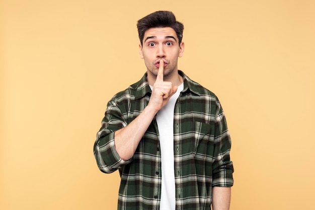 Uomo che fa un gesto di silenzio con l'indice indossando una camicia a scacchi e guardando direttamente la telecamera