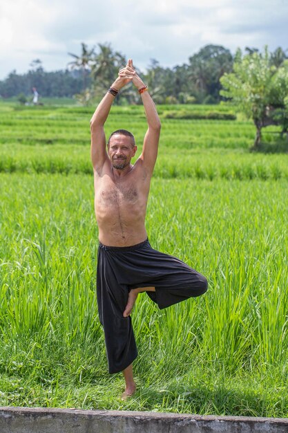 Uomo che fa yoga e medita in una posizione vicino a una terrazza di riso verde sull'isola tropicale di Bali Indonesia Primo piano