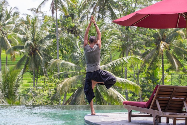 Uomo che fa yoga e medita nella posizione dell'albero vicino alla piscina sull'isola tropicale Bali Indonesia