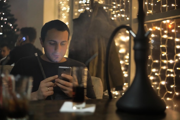 Uomo che fuma la pipa di narghilè in un bar notturno