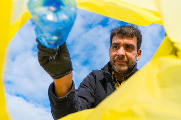 Uomo che getta una bottiglia in un sacco della spazzatura sulla spiaggia Ecologia Inquinamento del mare