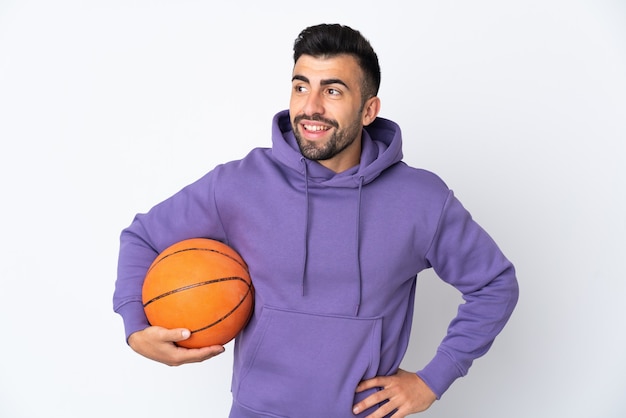 Uomo che gioca a basket sul muro bianco in posa con le braccia al fianco e sorridente
