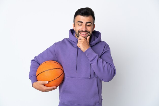 Uomo che gioca a basket sul muro bianco isolato che guarda al lato e sorridente