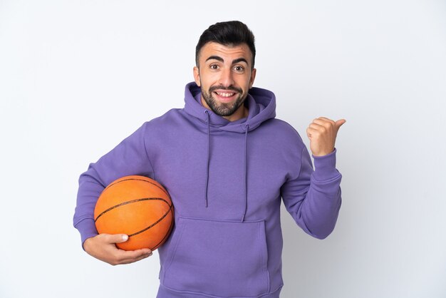 Uomo che gioca a basket sul muro bianco isolato che punta di lato per presentare un prodotto