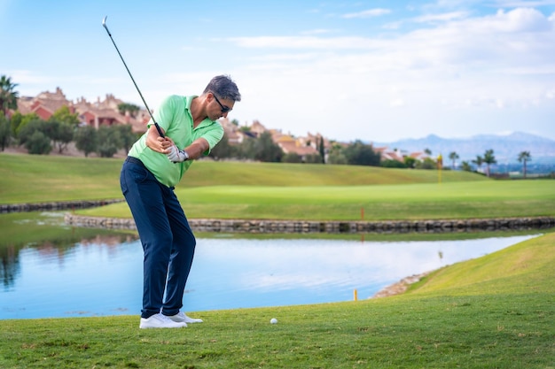 Uomo che gioca a golf al golf club vicino a un lago che colpisce la palla con il ferro o lanciando