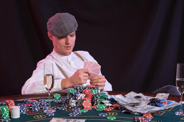 Uomo che gioca a poker al casinò seduto al tavolo con pile di chip denaro champagne carte backgr nero