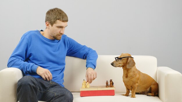 Uomo che gioca a scacchi con un bassotto intelligente Cane addestrato fa un gioco intelligente con il proprietario