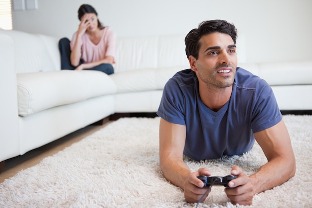 Uomo che gioca ai videogiochi mentre la sua ragazza si sta arrabbiando con lui