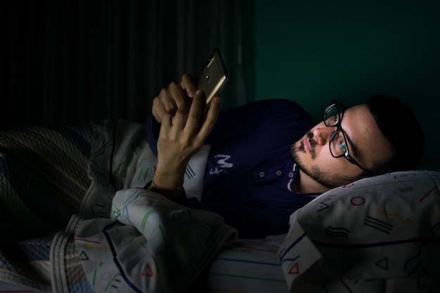 Uomo che guarda il suo telefono cellulare nel letto di notte