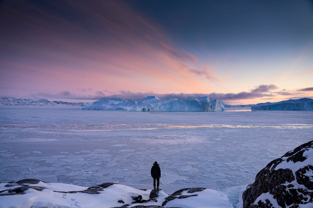 Uomo che guarda il tramonto sul mare ghiacciato in Groenlandia