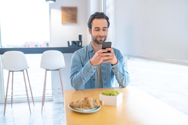 Uomo che guarda lo smartphone seduto al tavolo