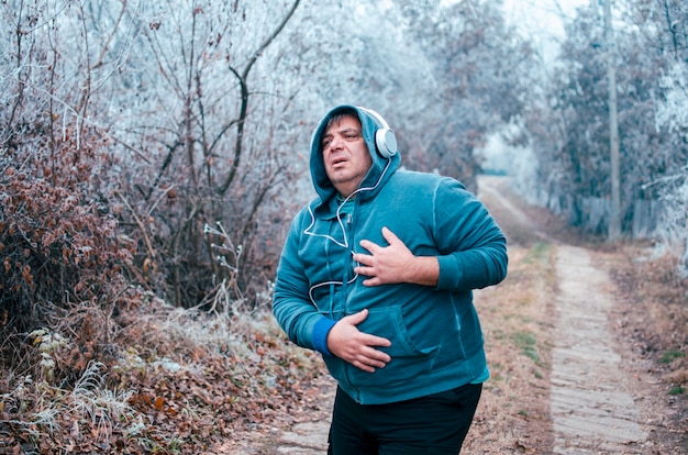 Uomo che ha infarto o insufficienza cardiaca dopo l'esecuzione. Uomo stanco sovrappeso maturo sul jogging all'aperto