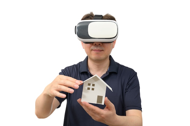 Uomo che indossa occhiali per realtà virtuale e tiene in mano una casa in legno isolata su sfondo bianco