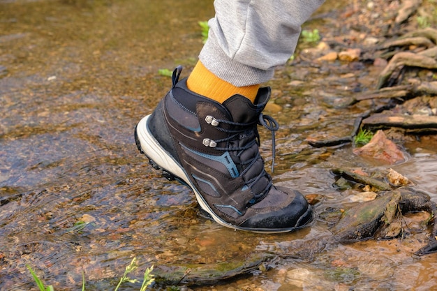 Uomo che indossa scarpe all'aperto e fa trekking in un parco fuori dal lago stivali nell'acqua del lago