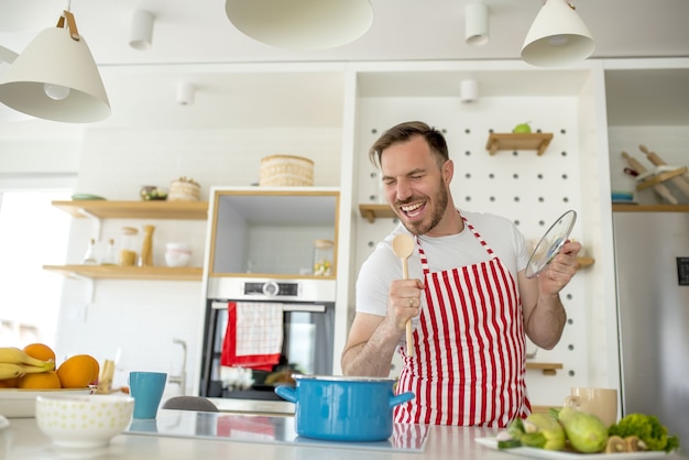 Uomo che indossa un grembiule bianco con linee rosse e cucina qualcosa in cucina