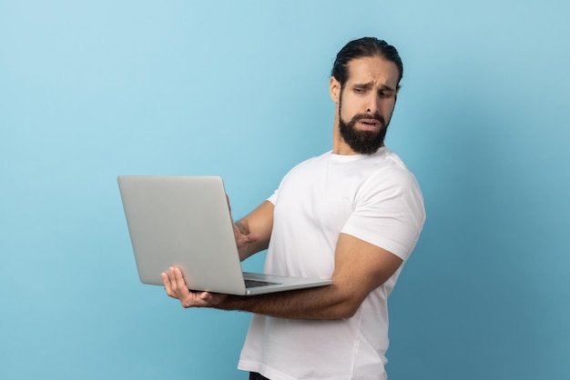 Uomo che indossa una maglietta bianca girando la faccia dal display perché non vuole vedere sullo schermo del laptop