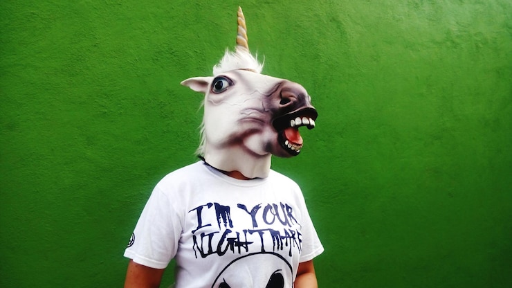Foto uomo che indossa una maschera da unicorno contro la parete verde