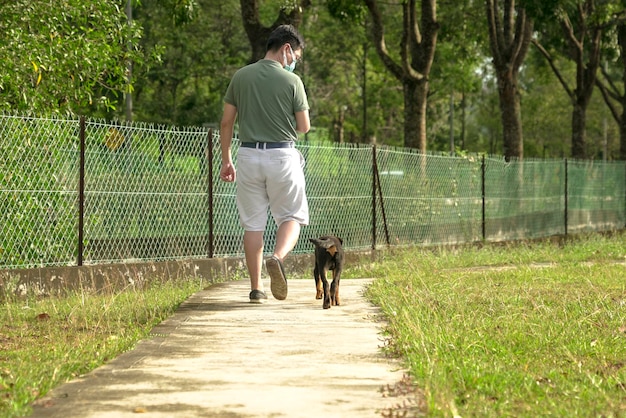 Uomo che indossa una maschera facciale che cammina con il cane al parco