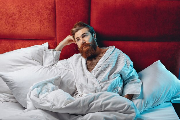 uomo che indossa una veste bianca e sdraiato a letto sotto una coperta bianca guardando verso l'alto sognando. Sogni notturni