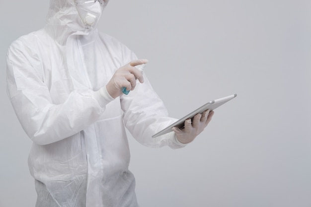 Uomo che indossa uniforme protettiva biologica, maschera e guanti disinfettante disinfettante su tablet