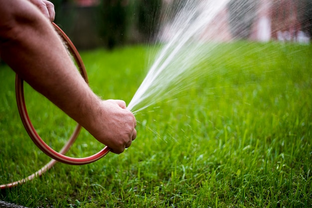 Uomo che innaffia giardino con tubo, close-up