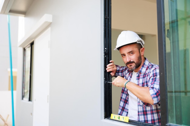 Uomo che installa finestre in un cantiere edile ispanico Lavoratore edile che indossa guanti protettivi e casco rigido