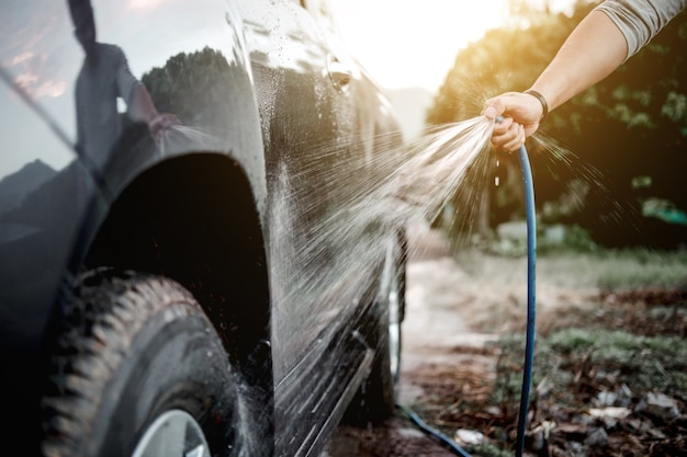 Uomo che lava e pulisce auto con acqua spruzzata sotto pressione