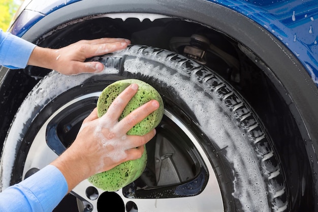 Uomo che lava le ruote dell'auto in autolavaggio Lavaggio auto