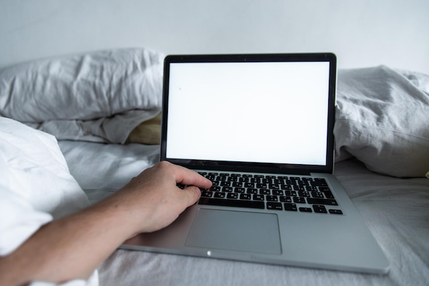 Uomo che lavora a letto sullo schermo bianco del computer portatile
