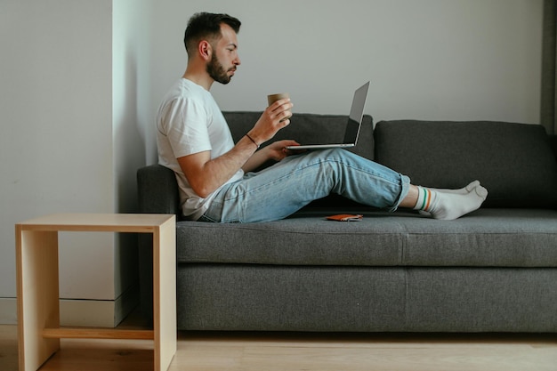 Uomo che lavora al portatile e beve caffè a casa
