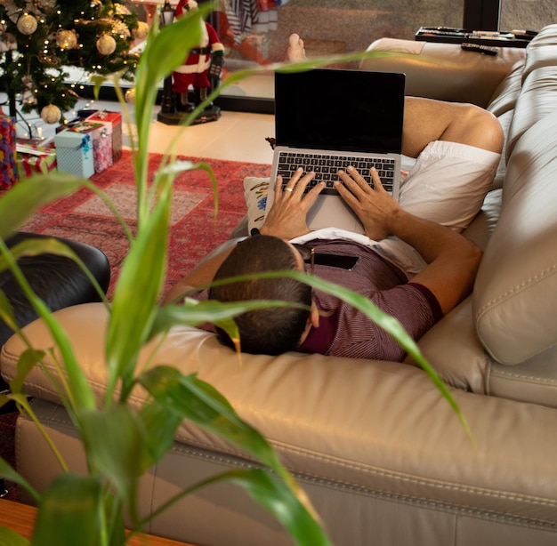 uomo che lavora da casa a natale sfondo con albero di natale sfocato