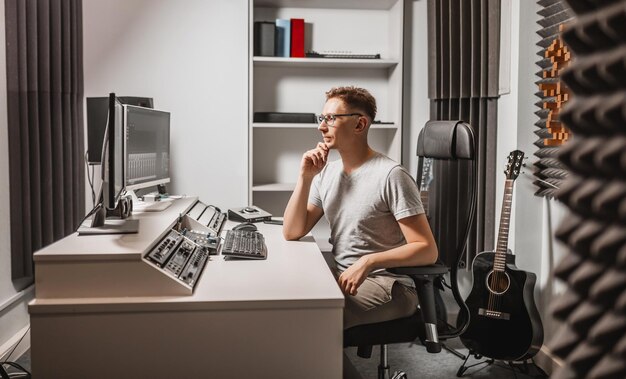 Uomo che lavora in uno studio musicale utilizzando il computer con gli occhiali Ingegnere del suono che lavora e pista di missaggio Programmatore che lo guarda durante l'ascolto della musica Concetto di tecnologia