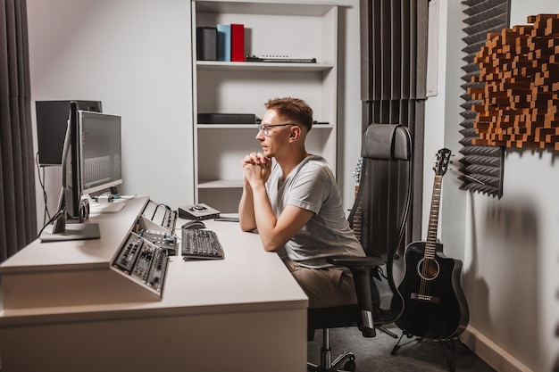 Uomo che lavora in uno studio musicale utilizzando il computer con gli occhiali Ingegnere del suono che lavora e pista di missaggio Programmatore che lo guarda durante l'ascolto della musica Concetto di tecnologia