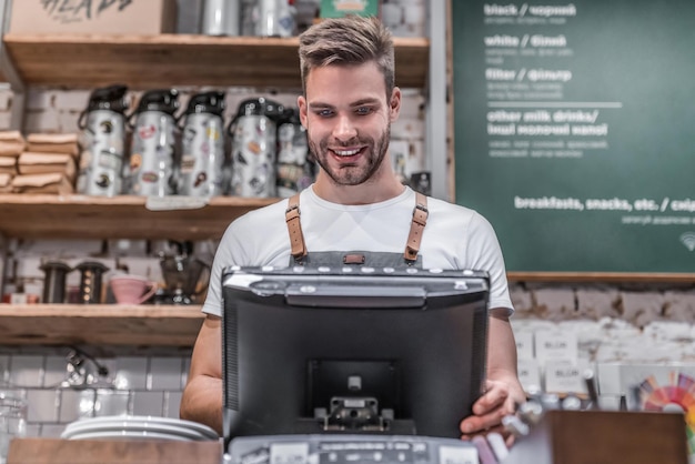 Uomo che lavora nella sua caffetteria al bancone con indosso un grembiule