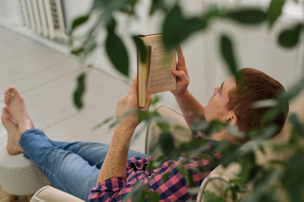 Uomo che legge tranquillamente un libro su una comoda sedia annidata tra il fogliame verde all'interno delle nature