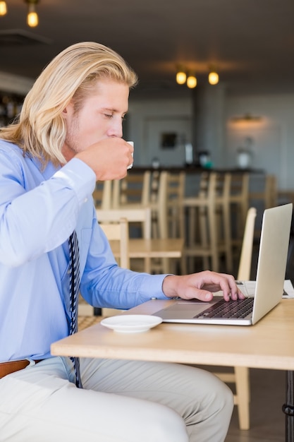 Uomo che mangia caffè mentre si utilizza il computer portatile