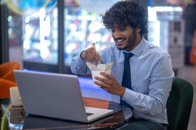 Uomo che mangia cibo giapponese sorridente al computer portatile